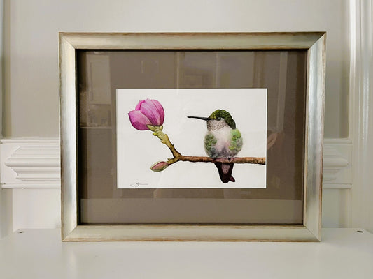 Framed watercolor artwork of a hummingbird and pink flower.