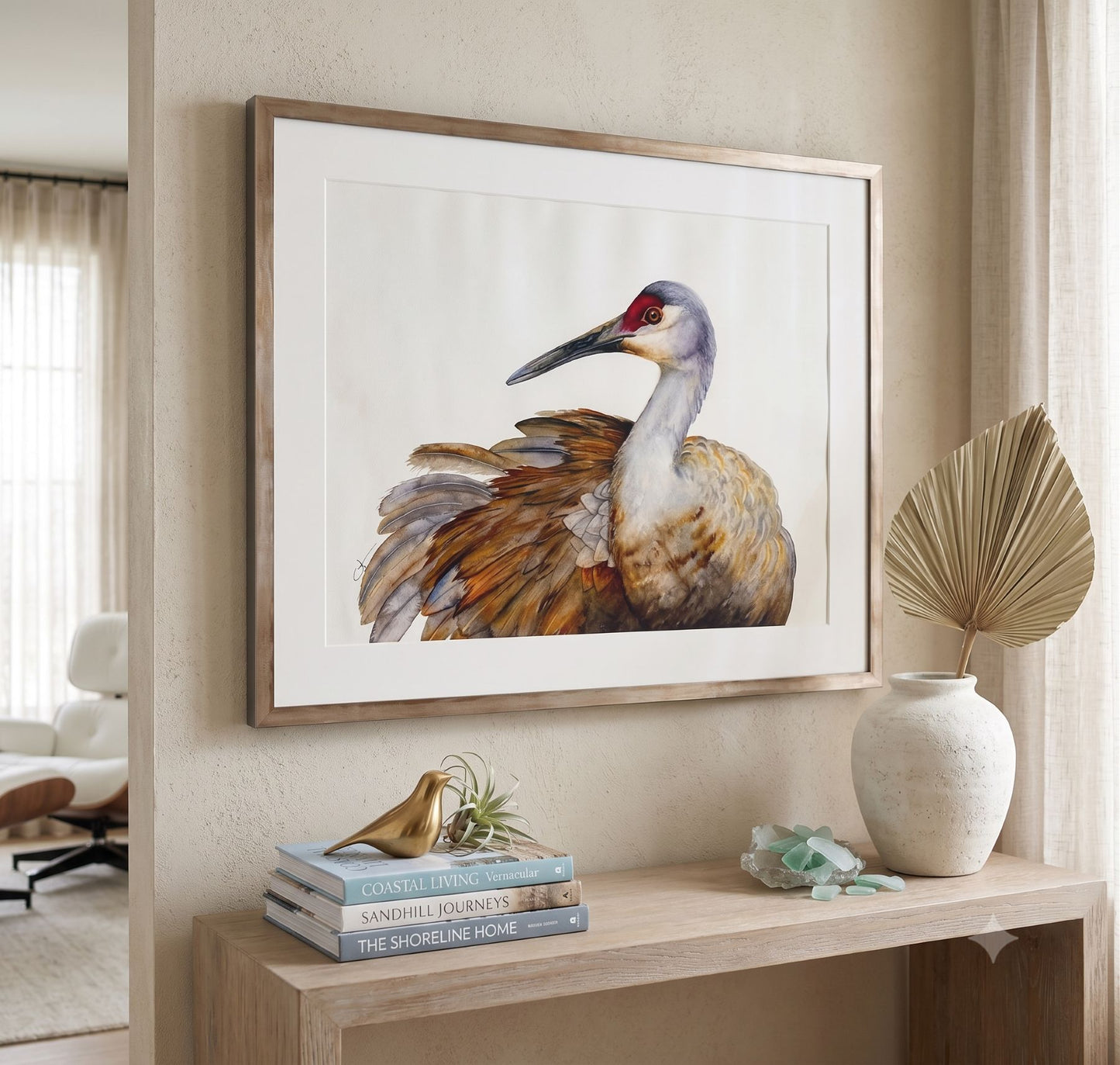 A framed watercolor painting of a sandhill crane by Vanessa Thorman hangs on a beige wall above a wooden console table in a styled interior. 