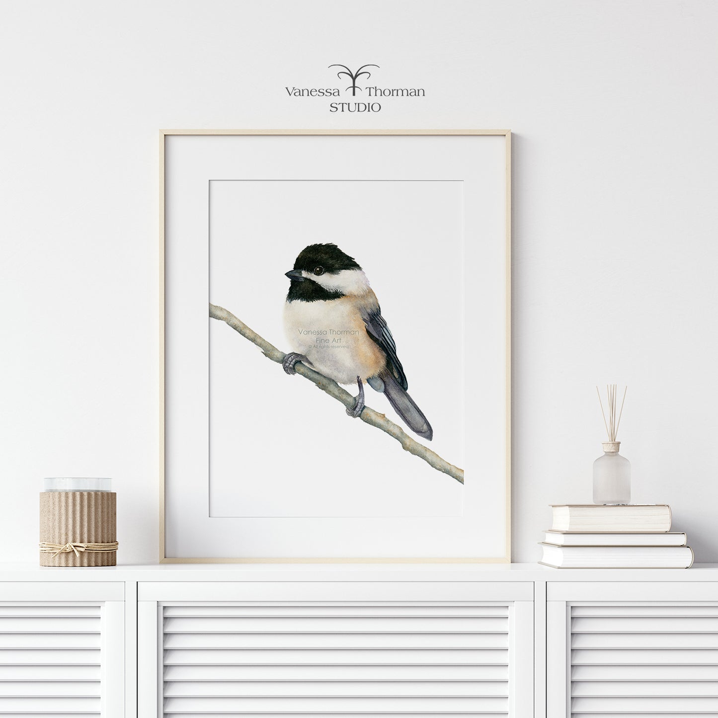 Framed Chickadee watercolor art print by Vanessa Thorman on a white console table
