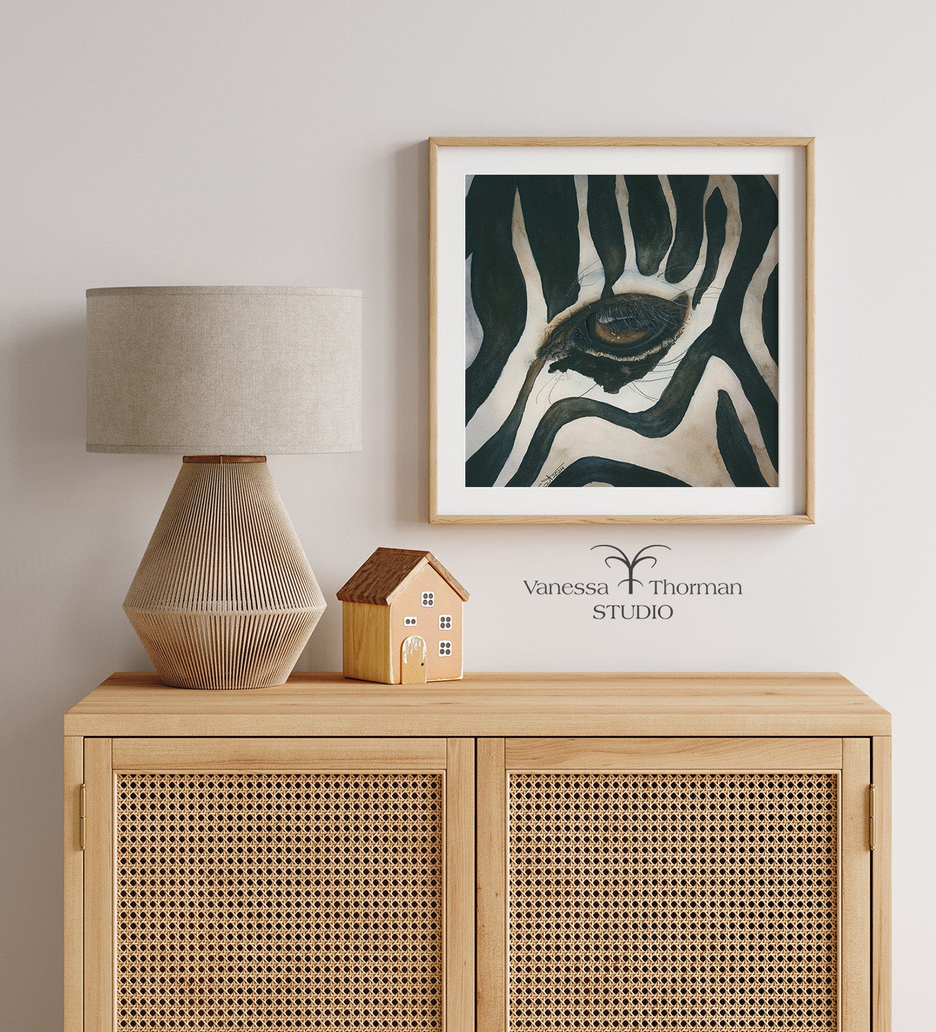 Framed "Eye of the Storm" zebra eye watercolor art print by Vanessa Thorman hanging over a wood hutch