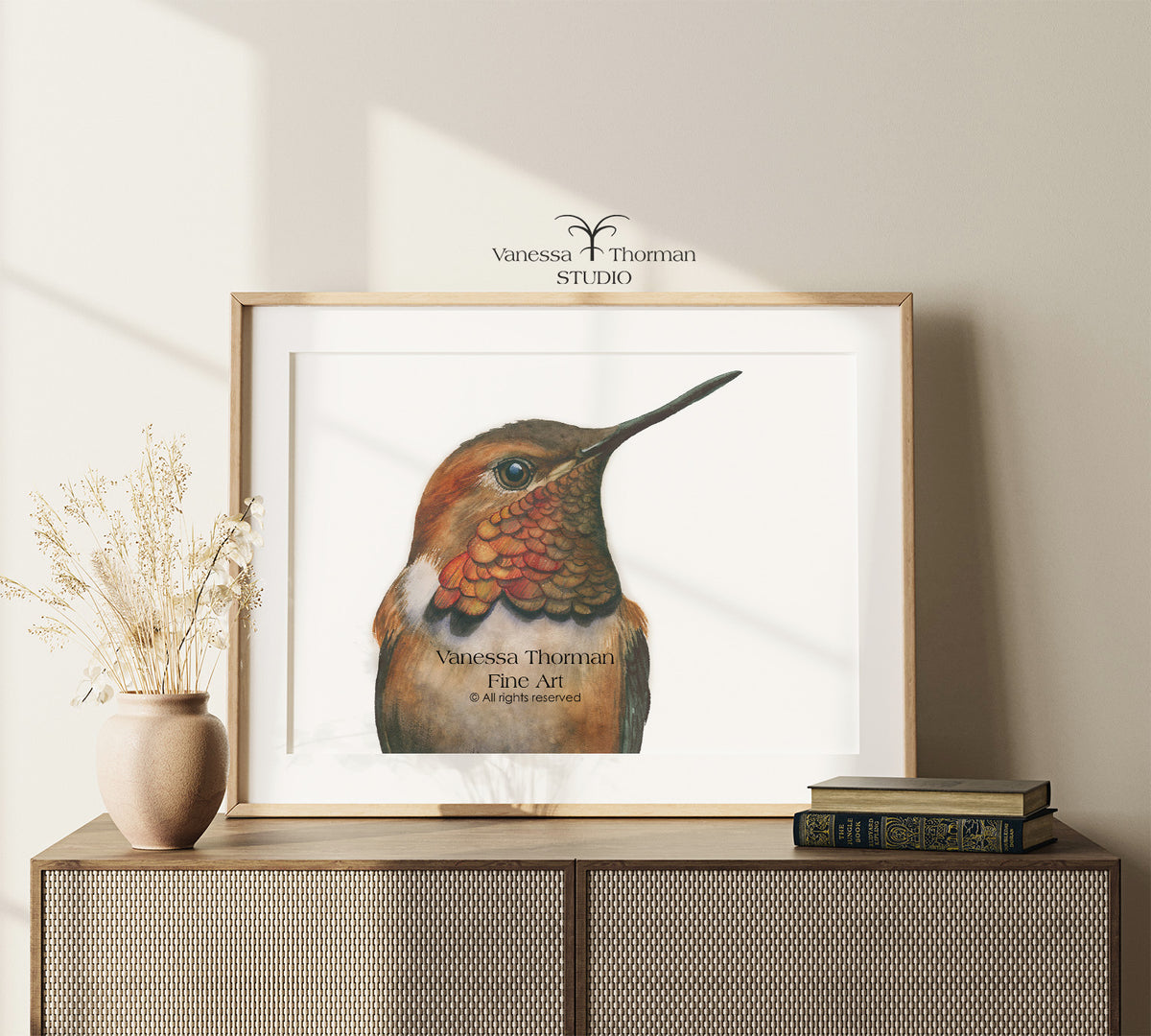 Framed "Rufous Hummingbird Portrait" watercolor art print by Vanessa Thorman on a console table