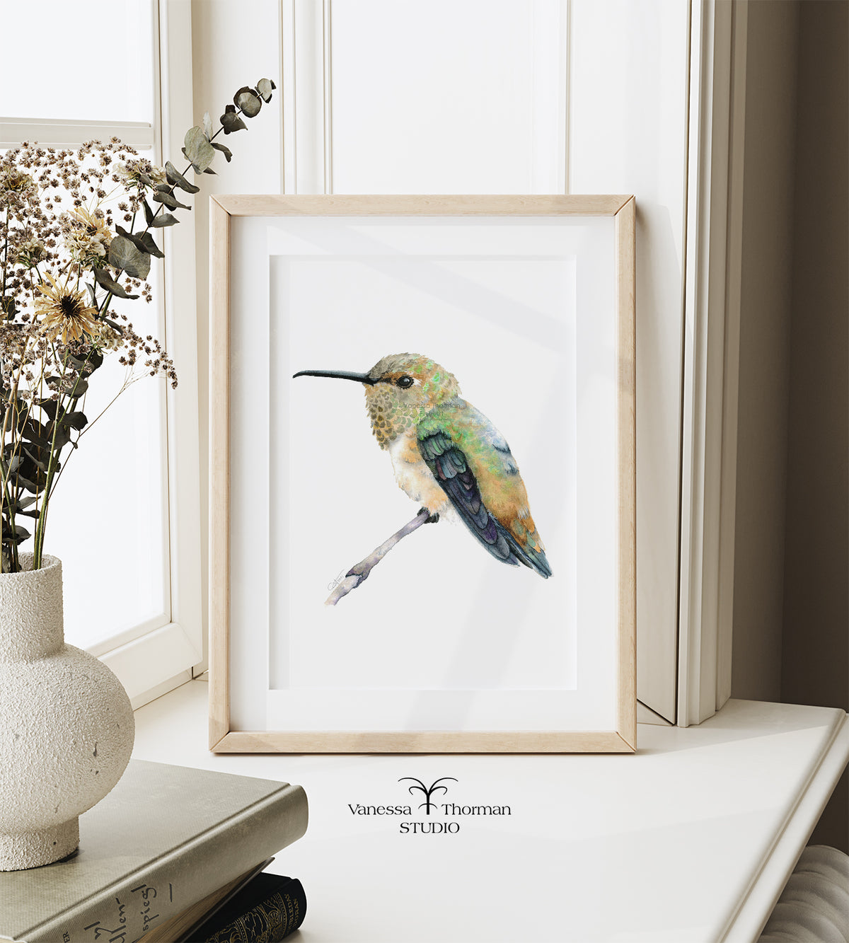 Framed Rufous Hummingbird watercolor art print by Vanessa Thorman displayed on a windowsill