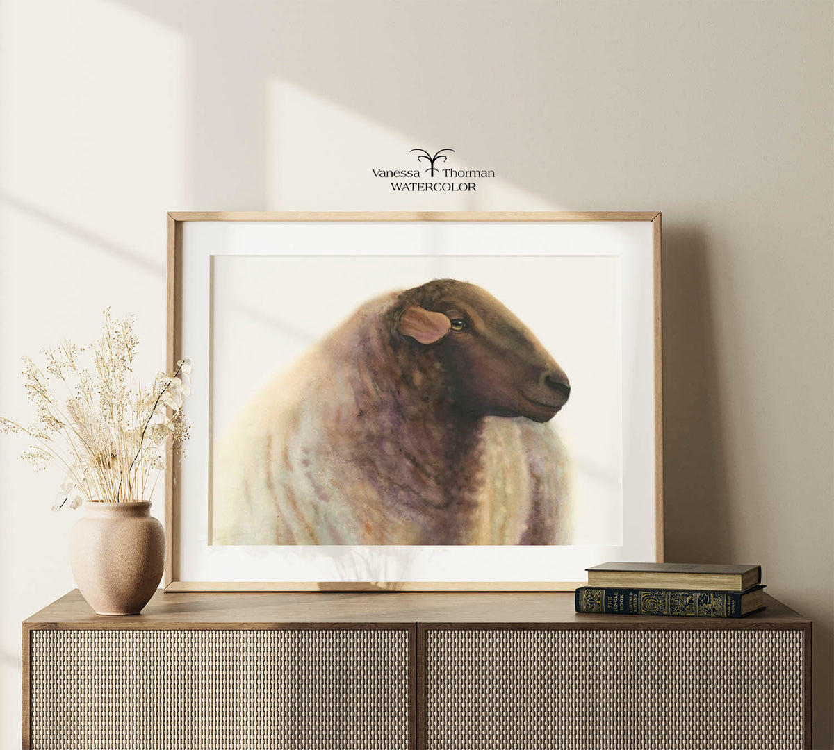 Framed "Theo" sheep watercolor art print by Vanessa Thorman displayed on a console table