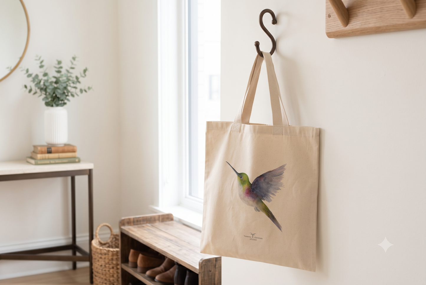 Vibrant hummingbird watercolor art canvas tote hanging from a hook inside a home