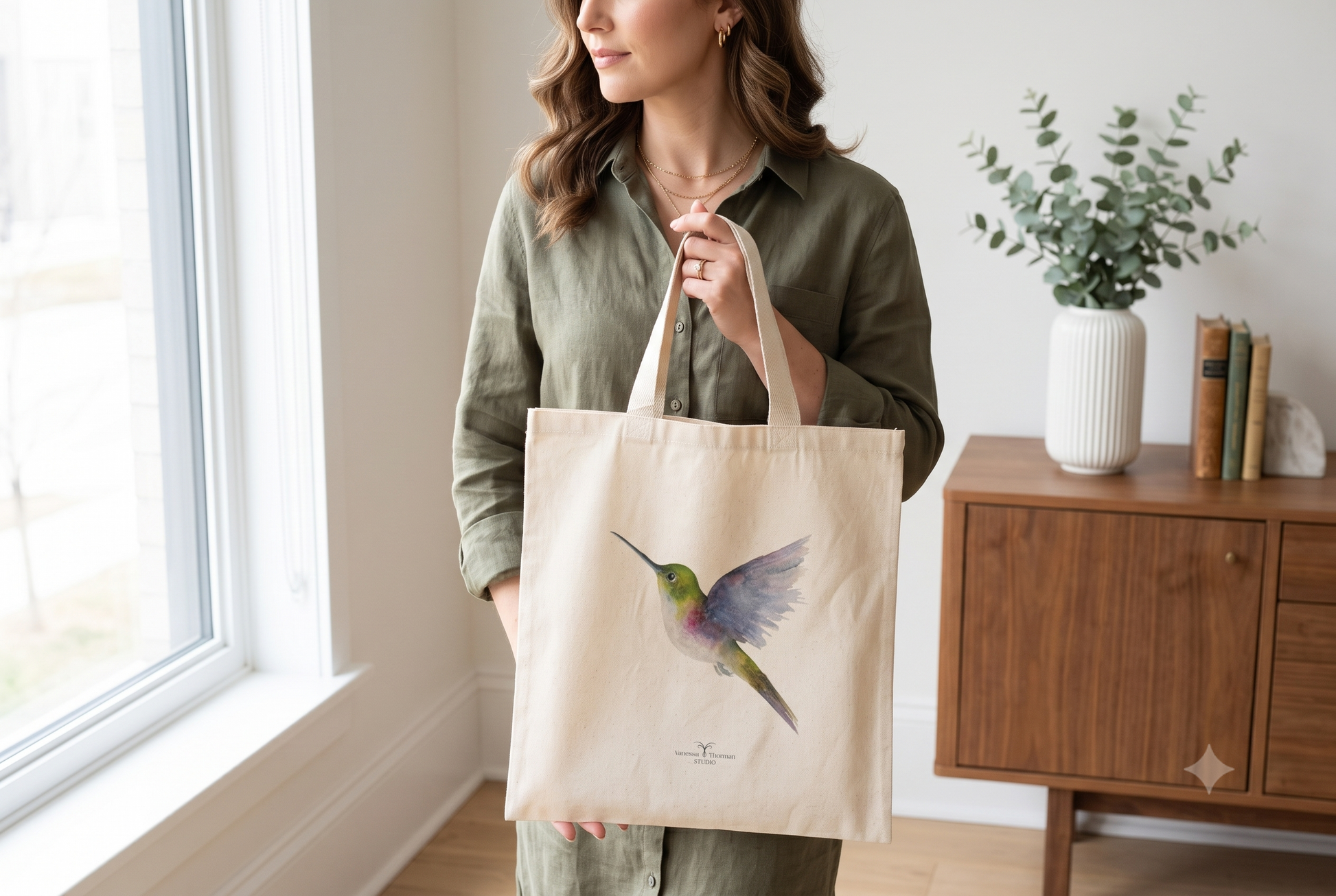 A woman holds a Vibrant hummingbird watercolor art canvas tote